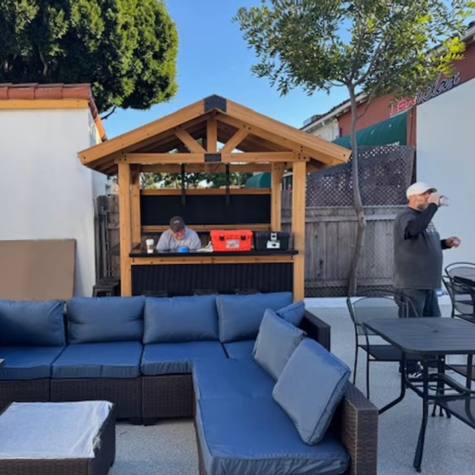 Outdoor patio with blue sectional seating, a wooden bar with a person, and another person drinking.