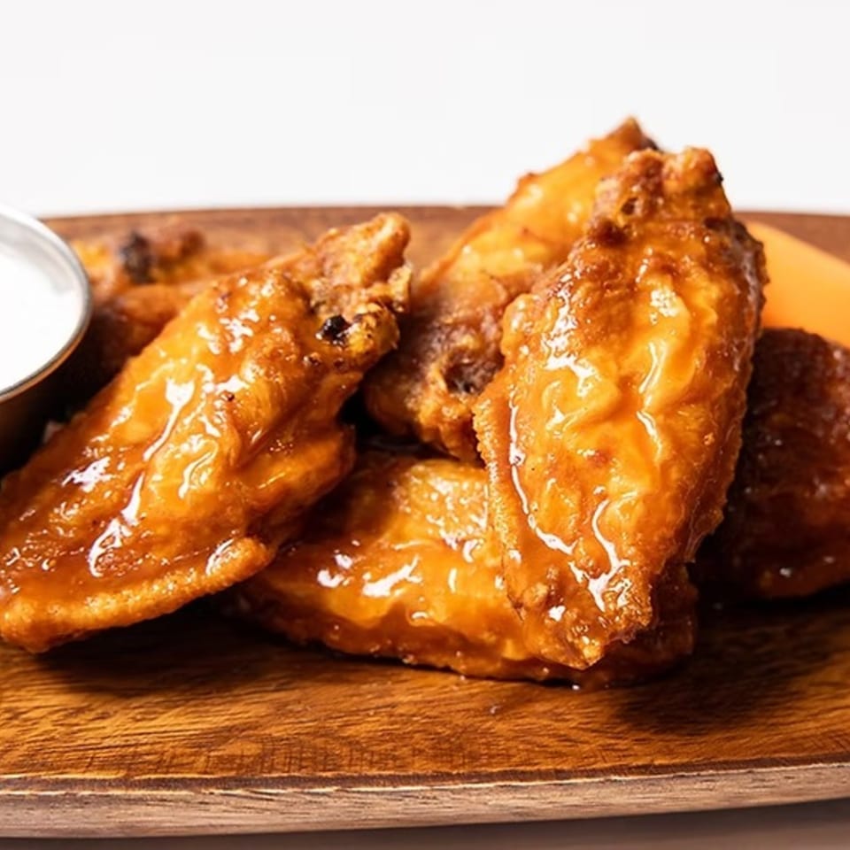 Close-up of several glazed chicken wings with a side of ranch dressing on a wooden board.