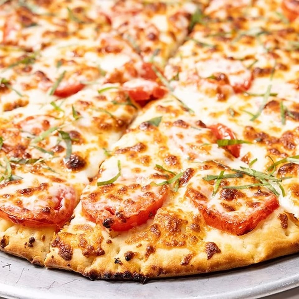 Close-up of a freshly baked Bob Cantu's pizza, topped with melted cheese, tomato slices, and basil.