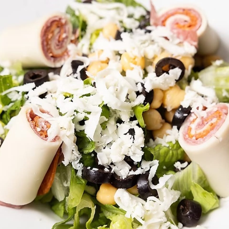 Close-up of a salad with rolled deli meats, shredded cheese, chickpeas, black olives, and lettuce.