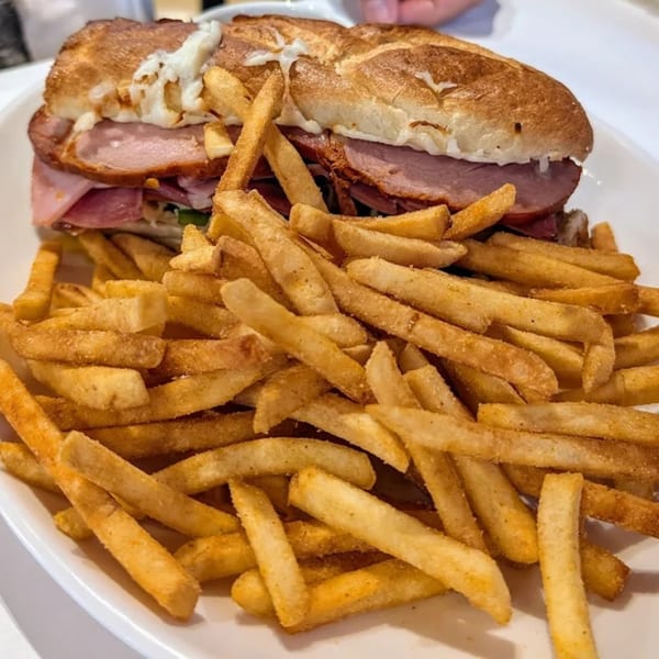 A large ham and cheese sandwich on a hoagie roll, served with a pile of golden french fries.