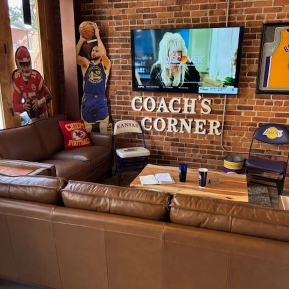 A sports bar lounge area with leather couches, a TV, and sports memorabilia on a brick wall.