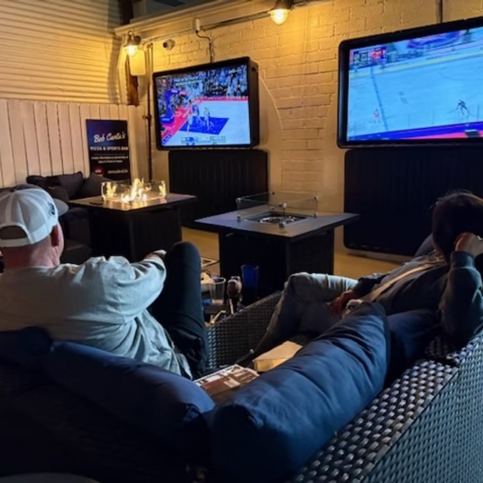 Two people relaxing on couches, watching sports on large screens at Bob Cantu's Pizza & Sports Bar.